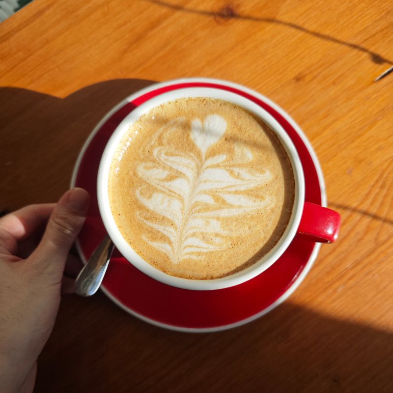 Taza roja de capuccino con latte art en mesa bellamente iluminada. Bebida estrella de Mafrens, cafetería de especialidad en Madrid.