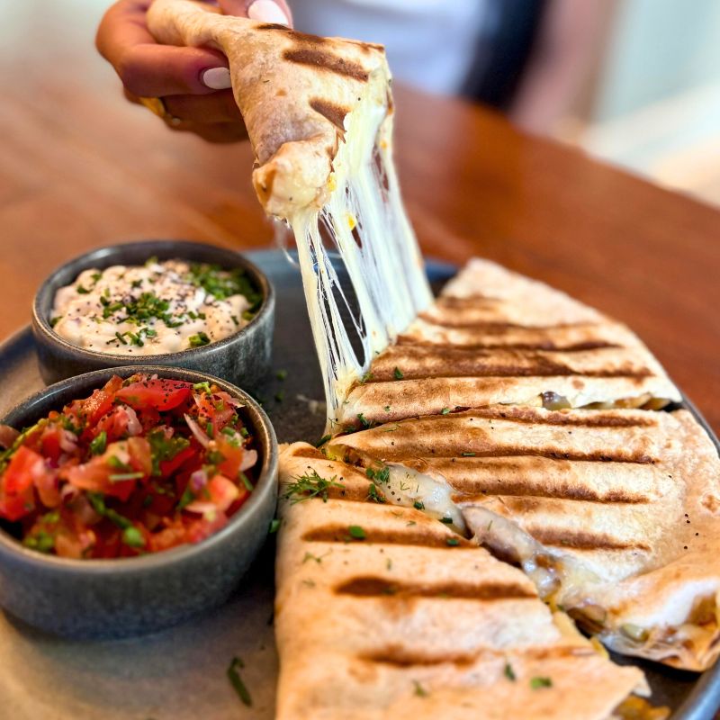 Quesadilla con abundante y suculento queso estirándose de una quesadilla a otra. Acompañado por pico de gallo y salsa cremosa.