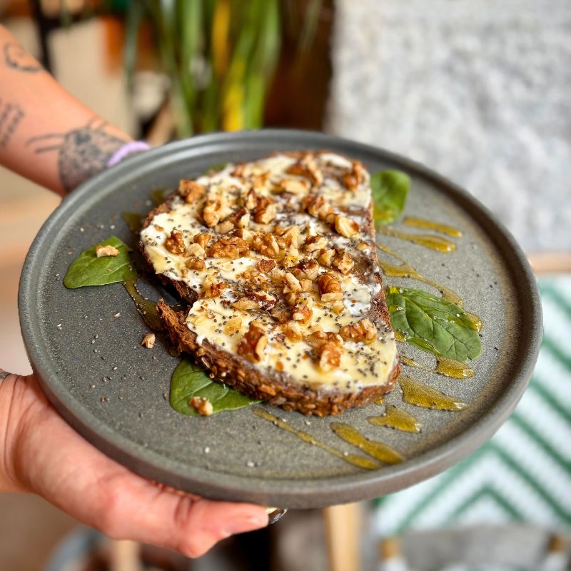 Manos de chica joven sujetando plato de tostada de queso mascarpone, coronado con nueces y miel.